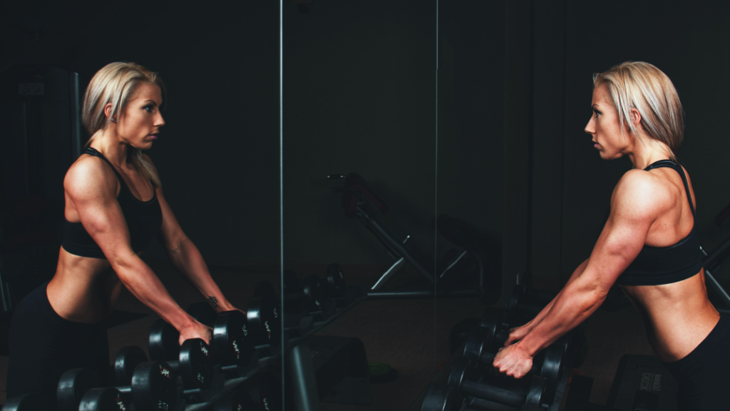 woman holding dumbbells looking in mirror