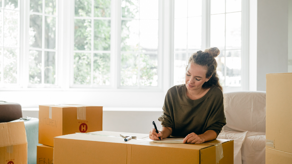 Woman writing on notepad surrounded by moving boxes